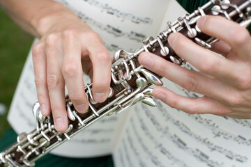 Close-up of a musician's hands playing a clarinet with a sheet music in the background