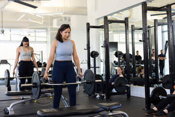 Confident woman lifting deadlift in gym surrounded by her piers