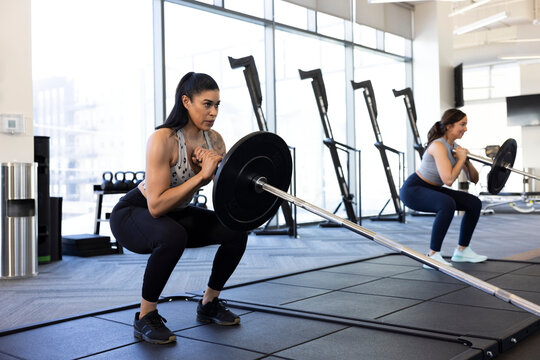 Woman taking a deep breath while doing barbell squats in gym