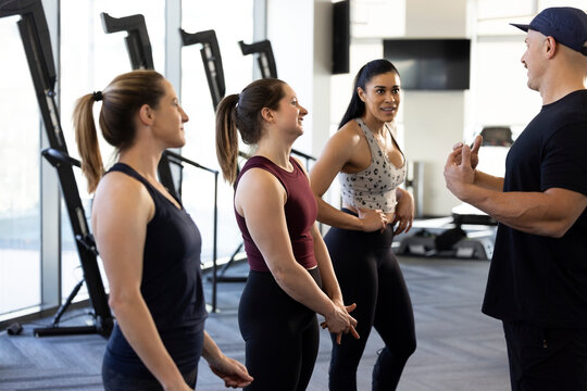 Three woman standing in a row listening to their fitness trainer before a workout - Powered by Adobe