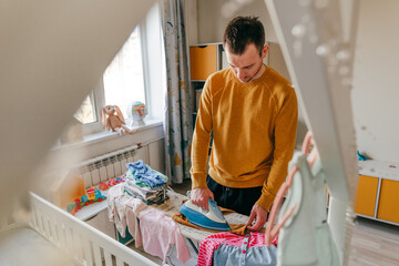 Young man ironing baby clothes in the children's room