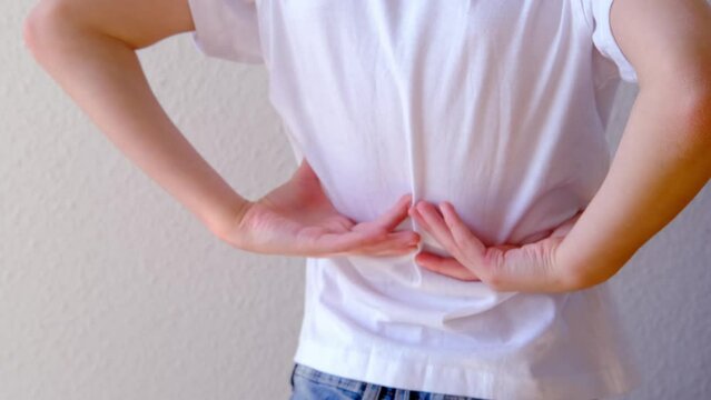 back of boy, child 8-10 years old in a white t-shirt grabbed a sore spot, curved spine, wrong posture, symbol of pain in spine, concept of osteochondrosis, scoliosis, back pain, intervertebral hernia