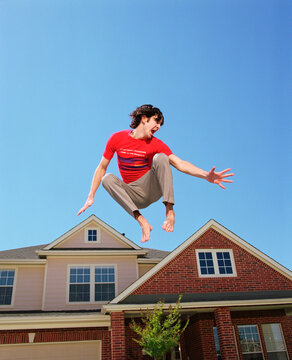 Teenage boy jumping in front of home, striking a pose mid air