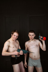 Two handsome shirtless guys with construction tools in their hands. Handsome gay couple with drill and screwdriver.