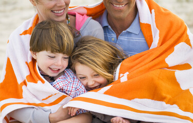 Family sitting at the beach with a towel wrapped around them