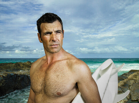 Close up portrait of man looking serious holding his surfboard at the beach