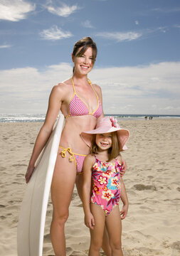 Mother holding surfboard and young daughter siling at the beach
