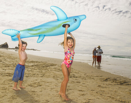 Young children holding up inflatable dolphin and laughing at the beach