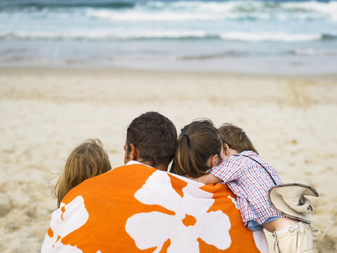 Family sitting at the beach with a towel wrapped around them