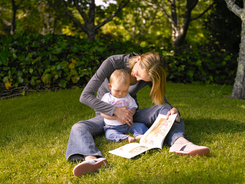 Mother sitting on the grass with little child reading a book to her