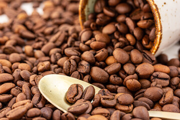 Roasted coffee beans, spoon, a ceramic cup. Macro, copy space