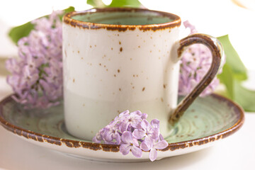 Composition with the branches of blossoming lilac flowers and a cup of coffee or tea on white background.  Spring background, selective focus