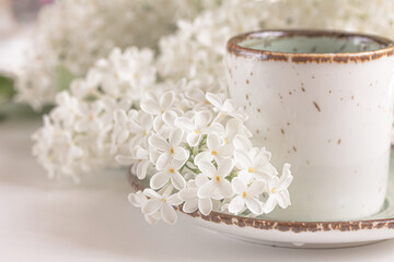 Obraz na płótnie Canvas omposition with the branches of blossoming white lilac and a cup of coffee or tea on white background. Spring background, copy space left