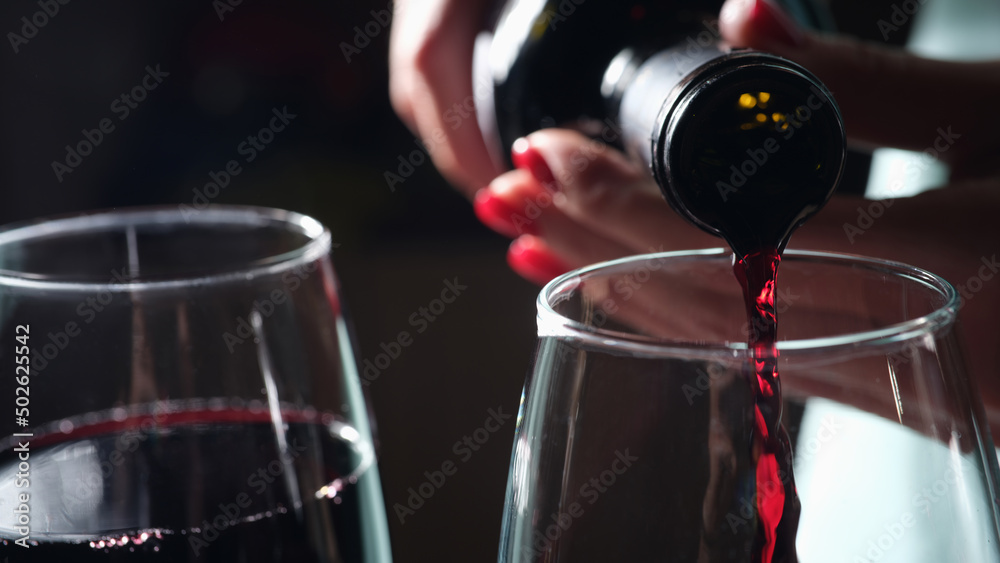 Wall mural Woman pours red wine into two glasses closeup