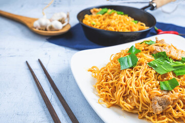 Stir noodles with vegetables in a white plate on a wooden floor.