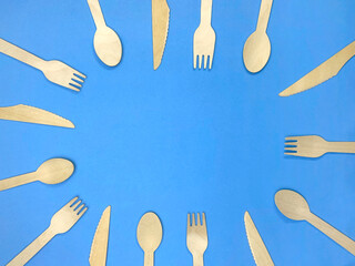 frame of wooden cutlery on a blue background. fork, spoon and knife made of eco-friendly materia