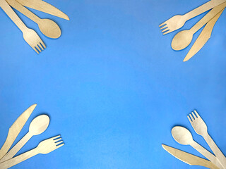 wooden cutlery on a blue background. fork, spoon and knife made of eco-friendly material. frame