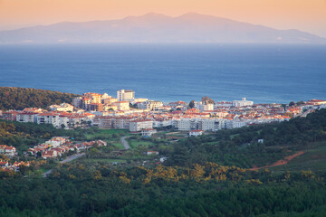 Obraz premium Cunda island view from top. Houses and green plants by the sea. Background, foggy evening time. Ayvalık, Balıkesir, Turkey