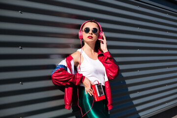 Back in time 90s 80s. Stylish girl in retro jacket and vintage cassette player listens to music, fashion trends, entertainment, heat in summer