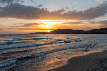 Sunset over empty beach, Elafonisos island, Greece. Small wave on wet sand, colorful cloudy sky