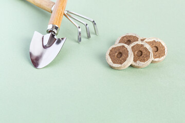 Peat briquettes for growing seedlings and young plants on a green background. Shovel, rake....