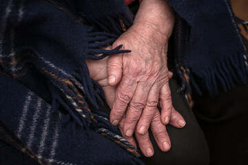 The hands of a mature 93-year-old grandmother with wrinkles lie on a cozy blanket at home. The...