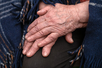 The hands of a mature 93-year-old grandmother with wrinkles lie on a cozy blanket at home. The...