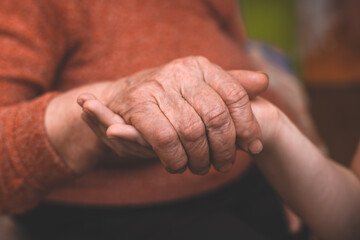 The grandson's hands hold the wrinkled hand of a sick elderly grandmother at home. The concept of...