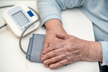 The hands of a mature 93-year-old grandmother with wrinkles are at home on a pressure measuring...