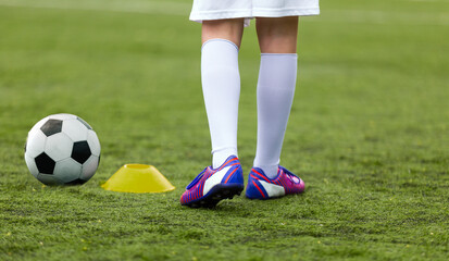 Fototapeta premium Closeup image of young football player kicking ball. School kids play sports outdoor. Soccer boy in white shorts and white soccer socks