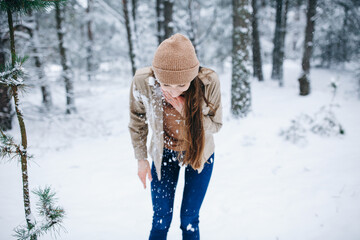 Fototapeta na wymiar beautiful young woman in a snowy winter forest. girl in a brown sweater and hat. walk in the winter forest and be very happy. snow-covered trees. stylish clothes 