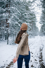 Fototapeta na wymiar beautiful young woman in a snowy winter forest. girl in a brown sweater and hat. walk in the winter forest and be very happy. snow-covered trees. stylish clothes 