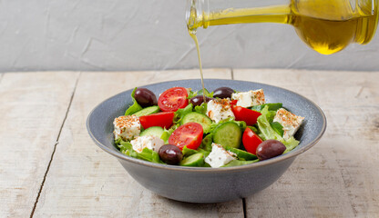 Italian or Mediterranean salad. Tomato cucumber feta leaves black olives and olive oil on wooden table.