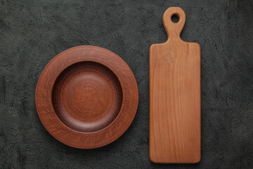 Brown wooden cutting board, empty brown clay plate on black stone table. Top view with copy space. Rustic dishes