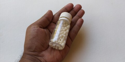 Hand holding fallen transparent glass bottle of small round indian homeopathy healthcare treatment...
