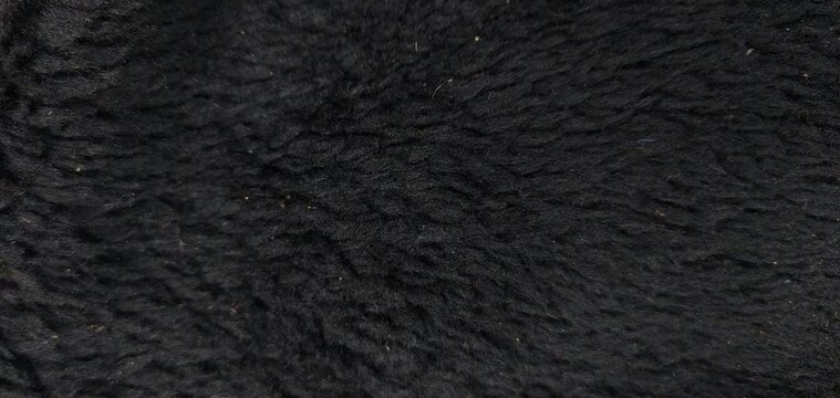 Smooth soft dirty black color furry, fluffy and hairy artificial sheep skin plush fur wool rug texture cloth knitted coarse background surface pattern for beauty and fashion concepts. Close up view.