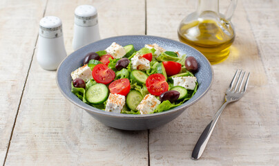 Fresh vegan salad from green leaves mix, vegetables, cheese, spices, olive oil and balsamic. Spring salad, healthy concept.  Wooden background