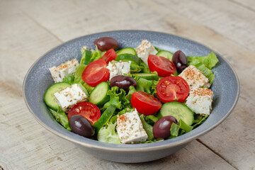 Fresh vegan salad from green leaves mix, vegetables and cheese. Spring salad concept.  Wooden background