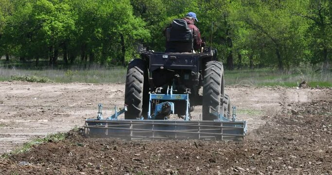 A peasant plows the land with a cultivator. A farmer in a tractor prepares the land with a sowing cultivator as part of pre-sowing work at the beginning of the spring season. Tractor processing field 