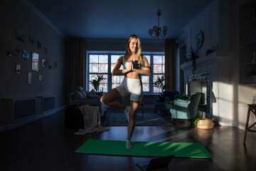 Fototapeta na wymiar Attractive woman doing yoga online using laptop at home.