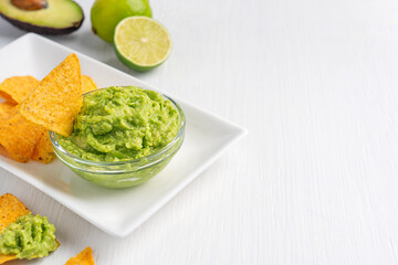Mexican guacamole homemade healthy vegetarian dip, spread, or salad made of mashed ripe green avocado served in glass bowl as snack or appetizer on white wooden table with lime. Image with copy space