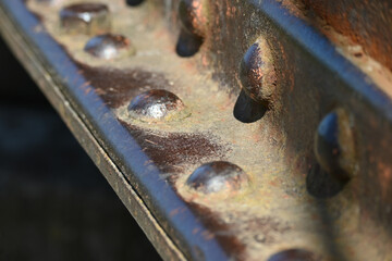 A fragment of an old rusty metal I-beam with rivets. Metal detail riveted with rivets close-up.