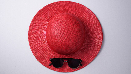 Red straw women's hat and black sunglasses centrally positioned on a white background. Summer flat...