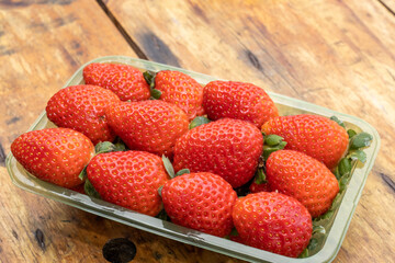 Red ripe strawberries in clear plastic tray, on wooden table