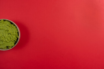 Top view of a ceramic bowl filled with the succulent guacamole sauce of Mexican origin on a red background