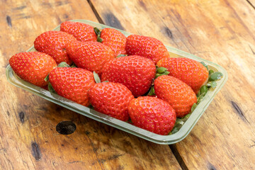 Red ripe strawberries in clear plastic tray, on wooden table