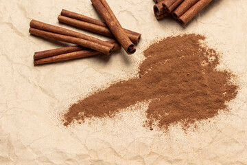 Ground cinnamon and cinnamon sticks on crumpled beige paper