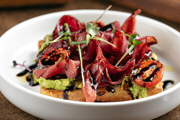 Closeup on breakfast toast with avocado and bresaola