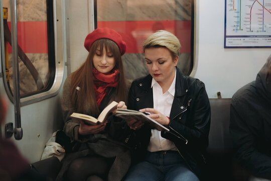 young caucasian women sitting in subway carriage in Saint Petersburg, Russia. One is reading a book, other looking at smartphone Image with selective focus, toning and noise effect