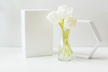 Geometric podium or pedestal with white spring tulips in a vase on a white background. Empty podium for product presentation